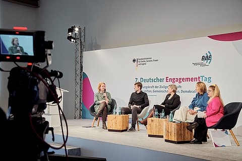 Fünf Personen sitzen auf der Bühne und werden gefilmt. Im Hintergrund die Logos von BMFSFJ und BBE
